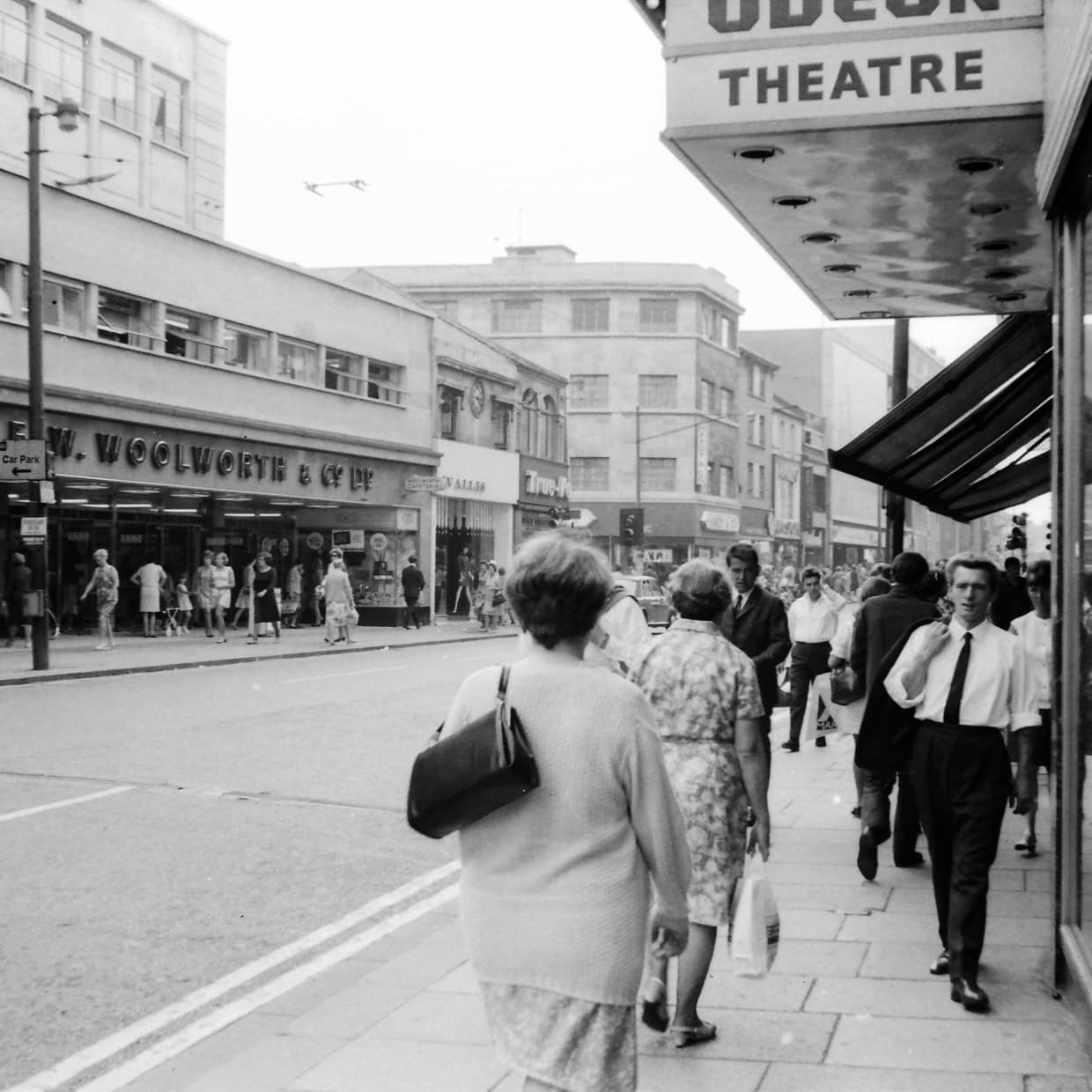 Black and white photo of a busy high street with Woolworths and Odeon Theatre signs.