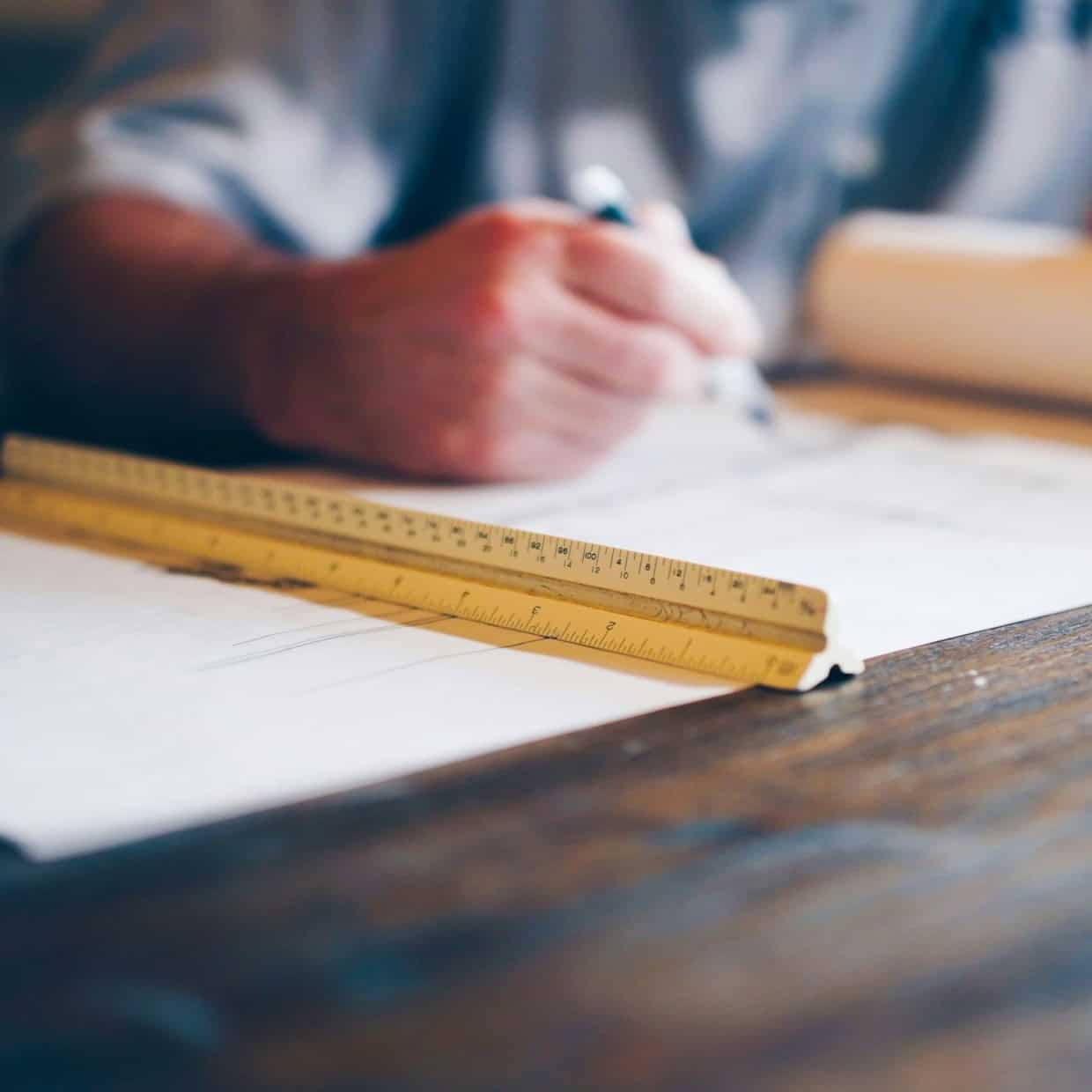 Architect working on building plans at a desk with a yellow ruler and pen in hand.