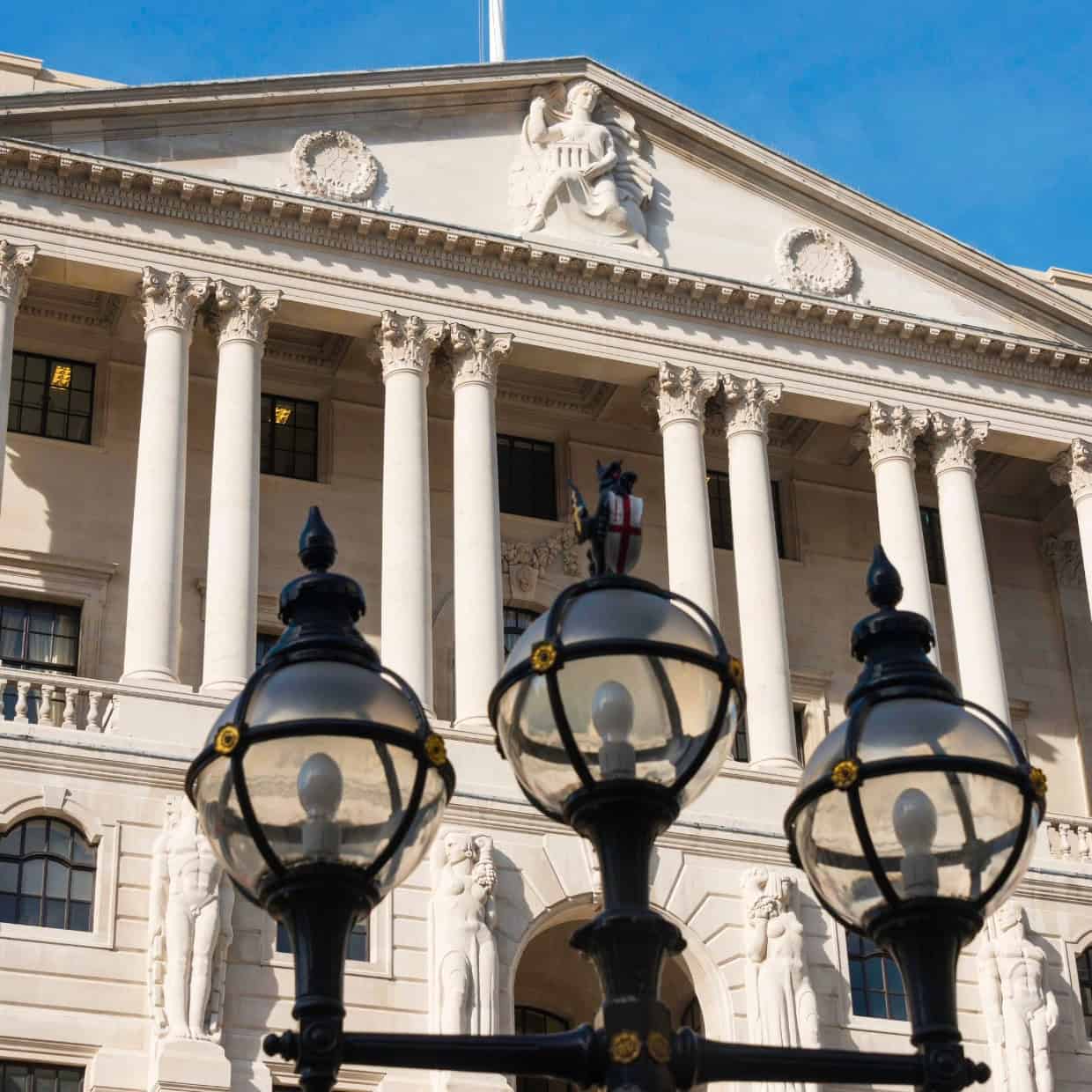 Grand neoclassical building with tall columns and statues, viewed from below with decorative street lamps in the foreground.