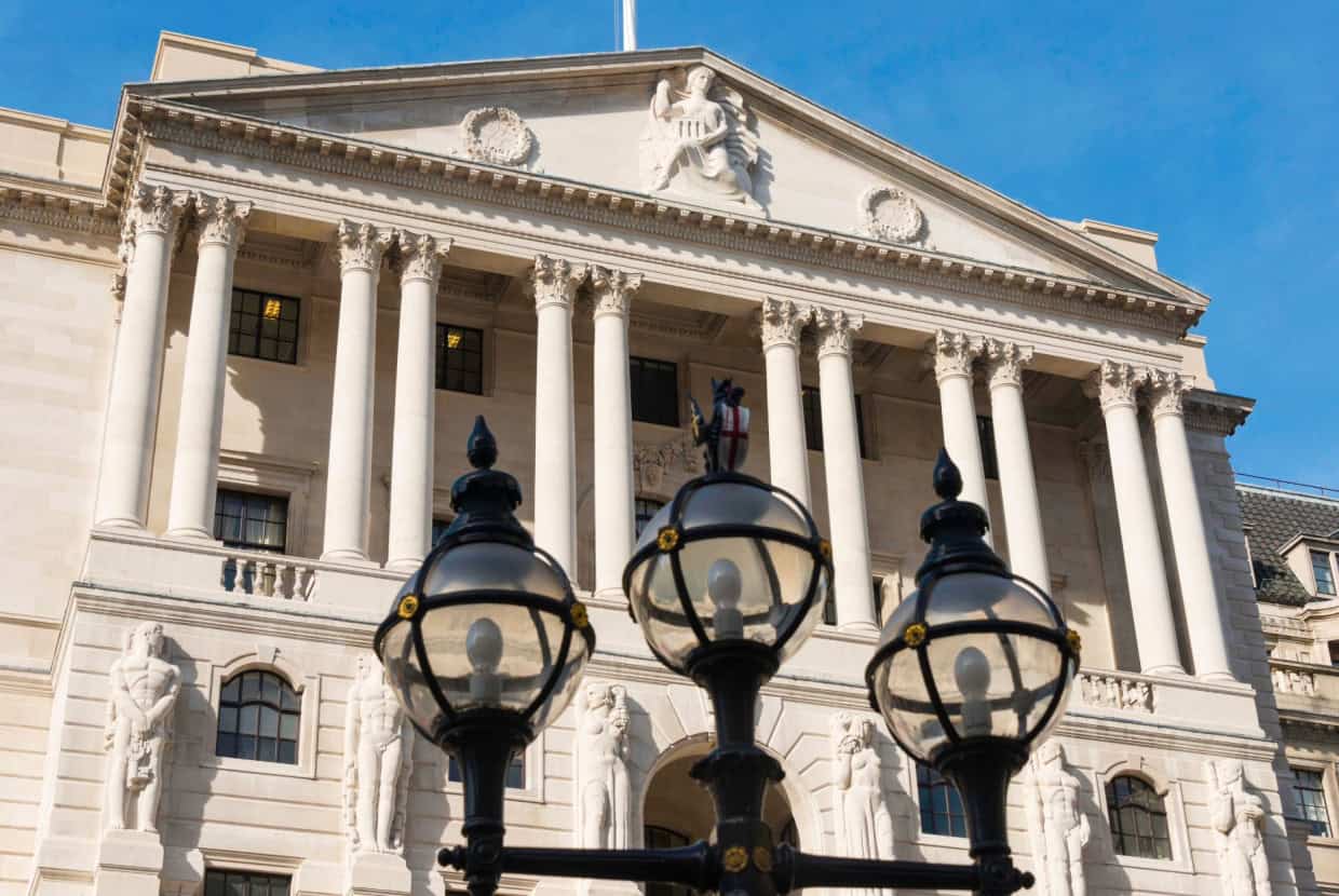 Grand neoclassical building with tall columns and statues, viewed from below with decorative street lamps in the foreground.