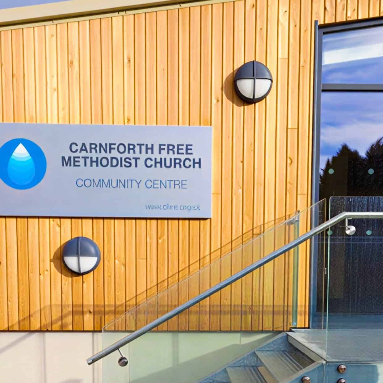 Sign for Carnforth Free Methodist Church community centre on a modern timber-clad building with glass entrance.