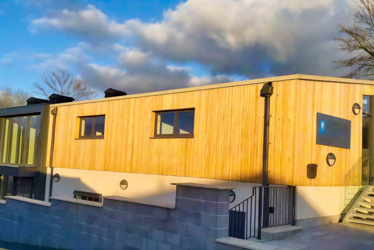 Contemporary building with timber cladding and windows, lit by warm sunlight under a cloudy sky.