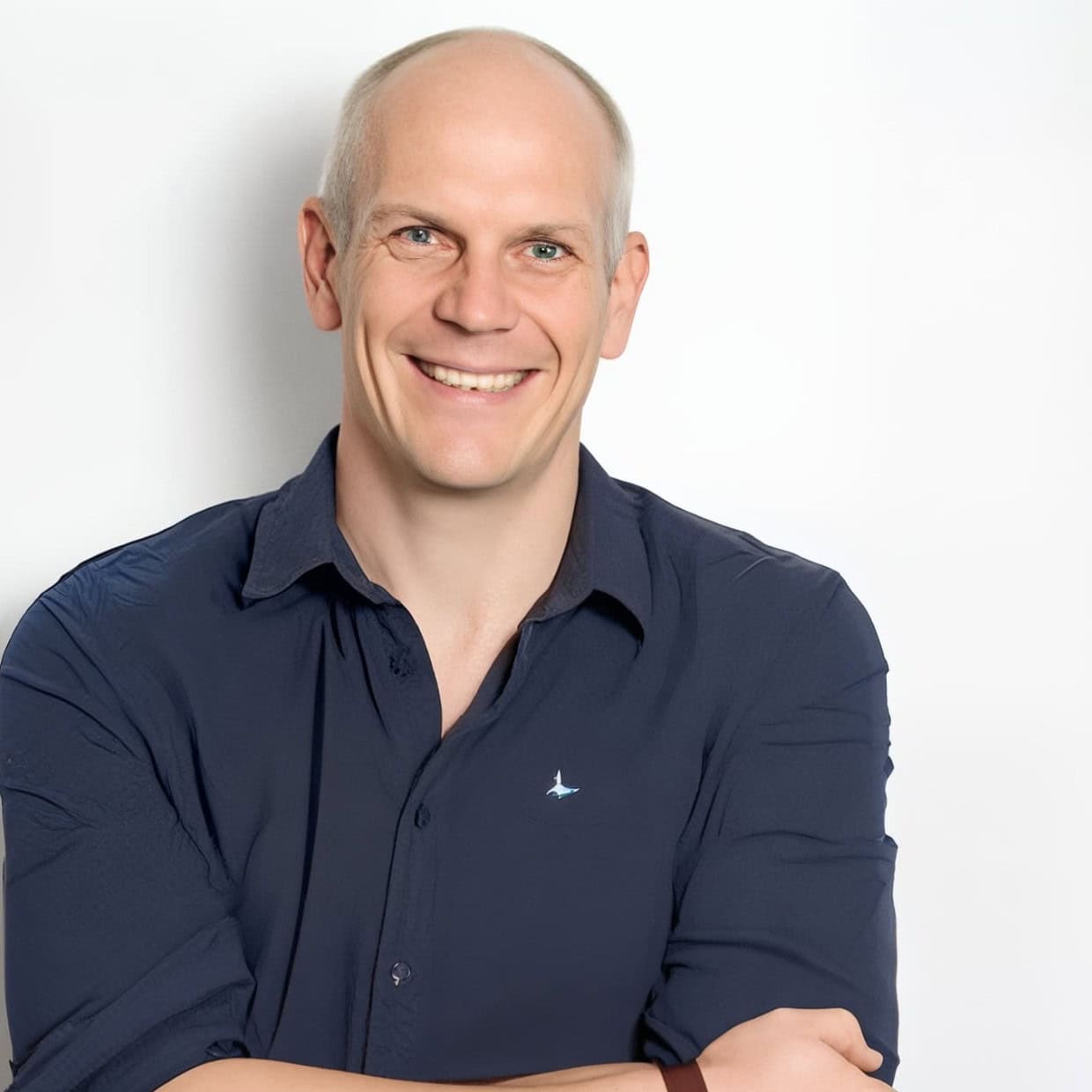 Smiling man in navy shirt with arms crossed against a light background, professional headshot.