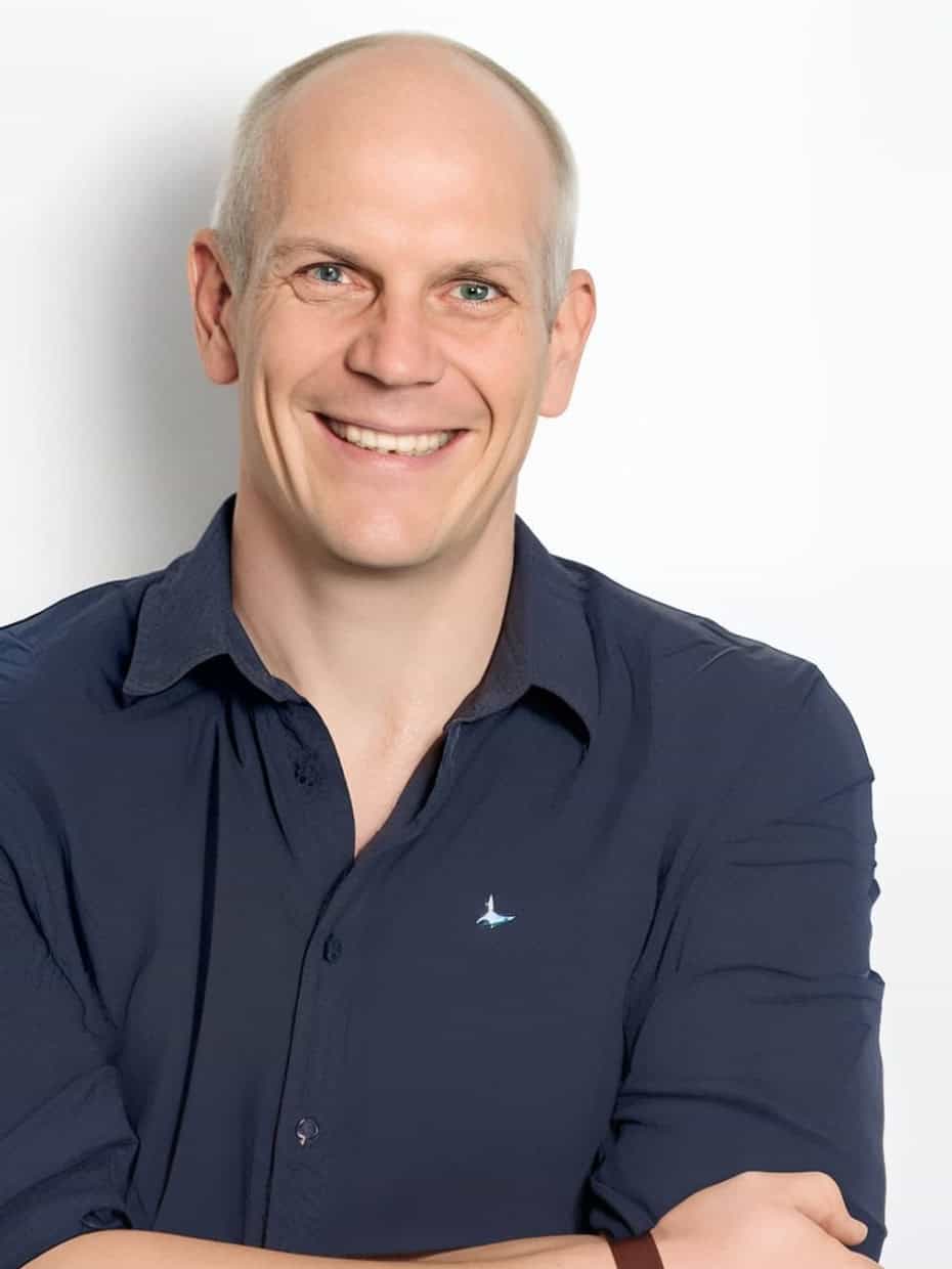 Smiling man in navy shirt with arms crossed against a light background, professional headshot.