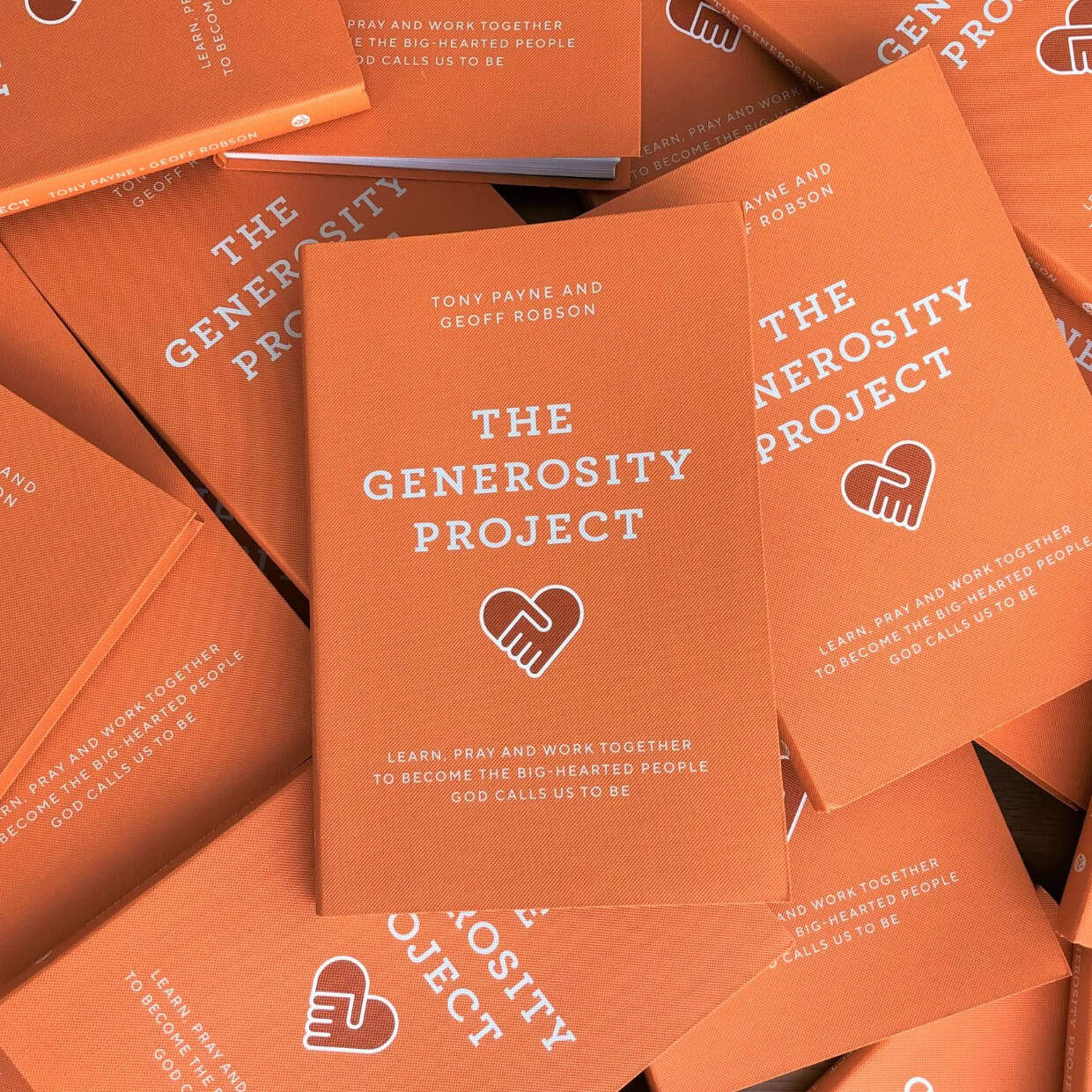 Multiple copies of The Generosity Project book with orange covers arranged in a stack.