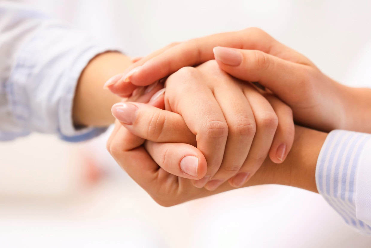 Close up of one person gently holding another person’s hands in a caring and supportive gesture.