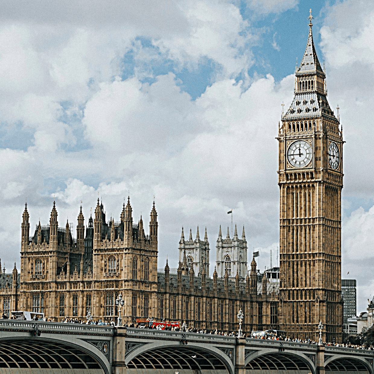 Elizabeth Tower (Big Ben) and the Houses of Parliament viewed from Westminster Bridge with people and traffic, under a cloudy sky in London.
