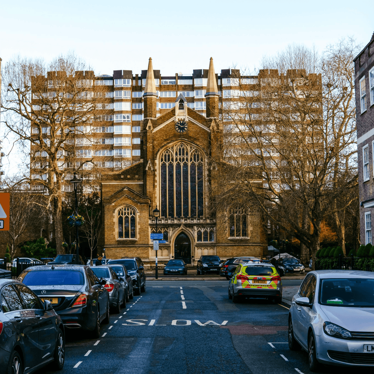 Historic church building at the end of a residential street with parked cars and modern buildings behind.
