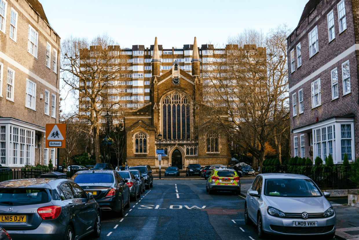 Historic church building at the end of a residential street with parked cars and modern buildings behind.