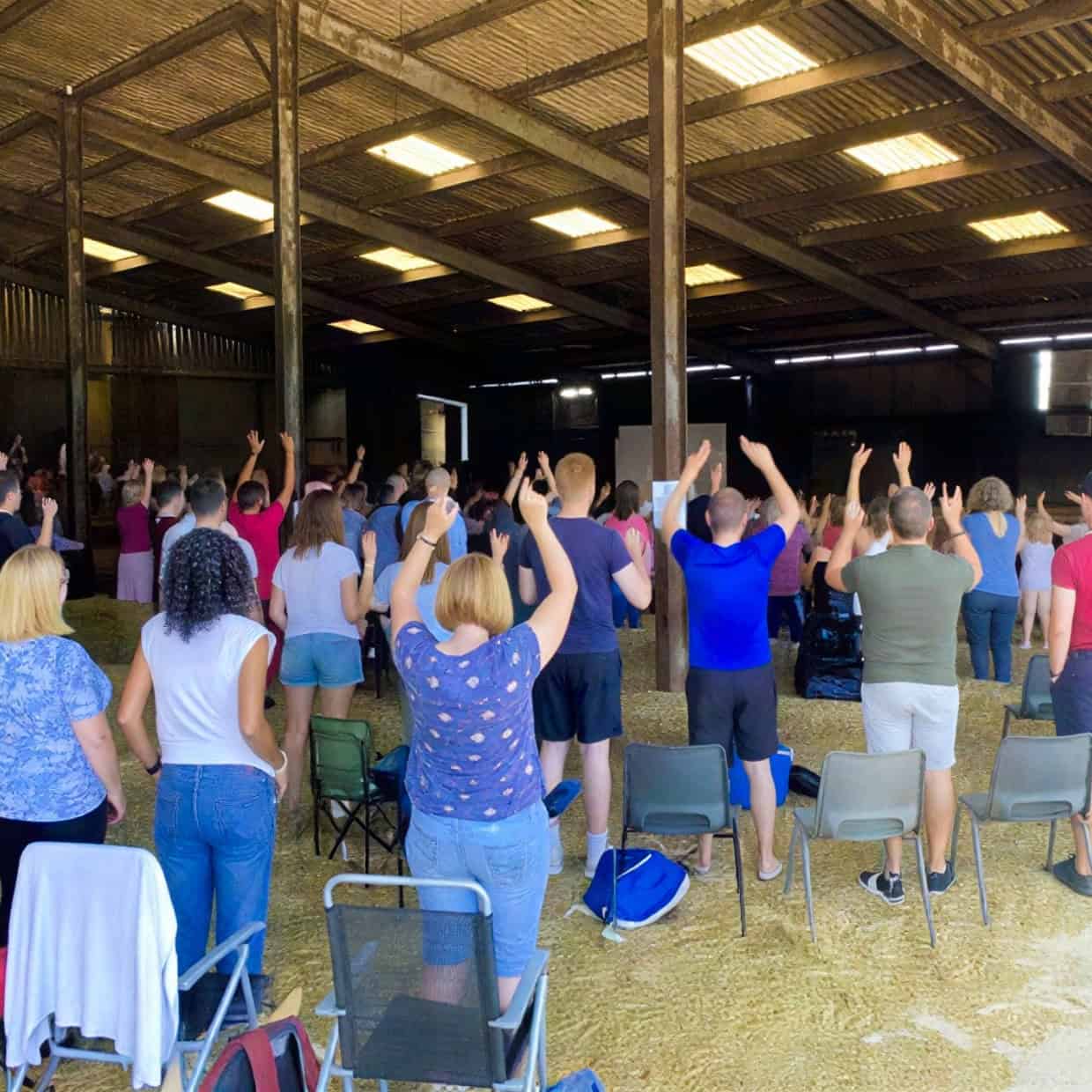 People gathered in a barn-style venue raising their hands during a church worship service.