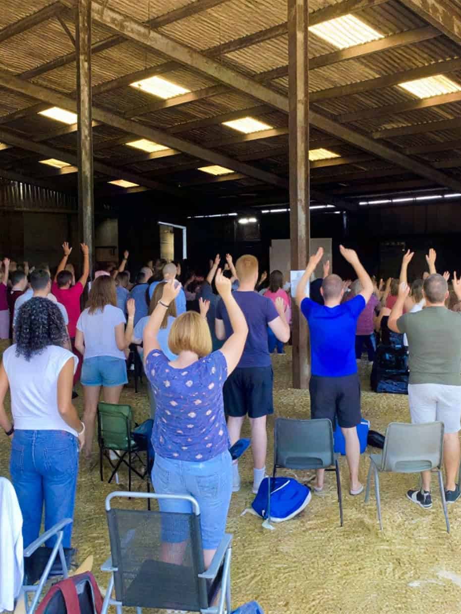 People gathered in a barn-style venue raising their hands during a church worship service.