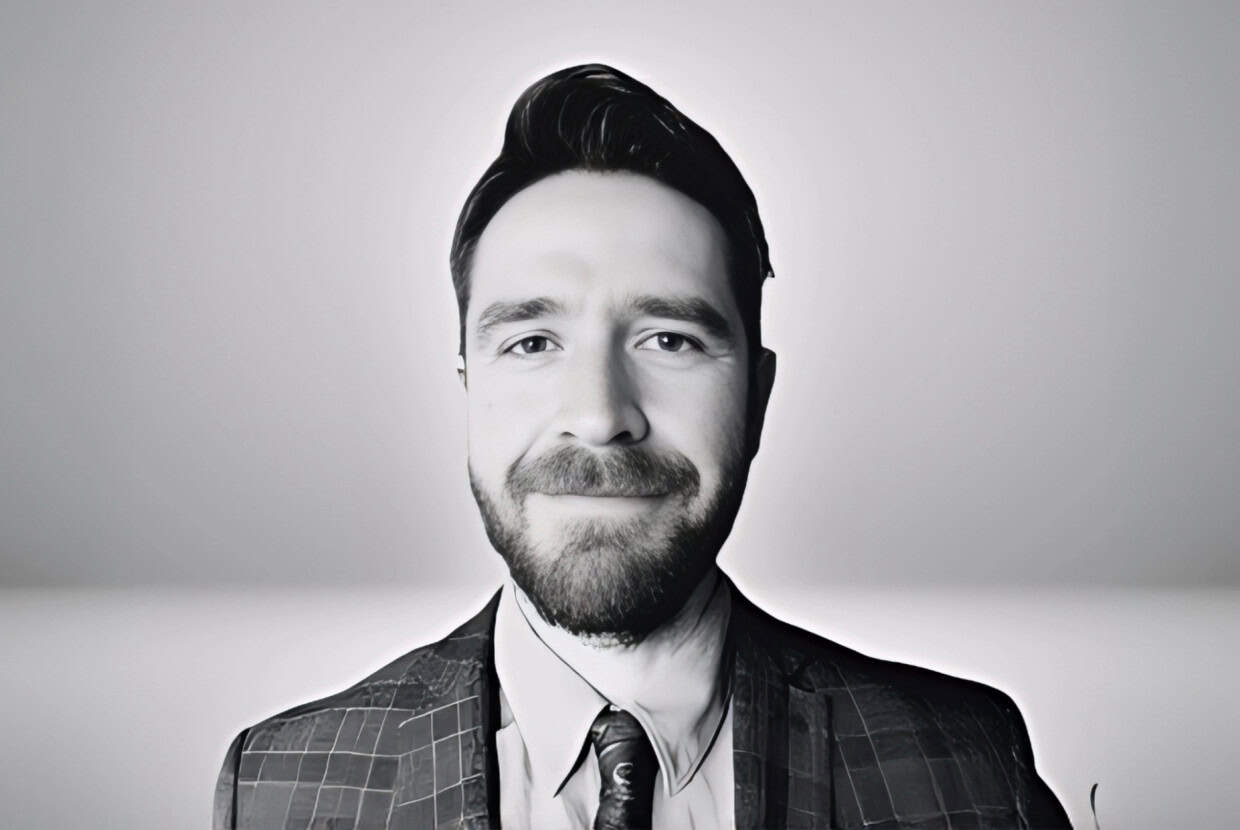 Black and white portrait of a smiling man in a patterned suit jacket and tie against a plain background.