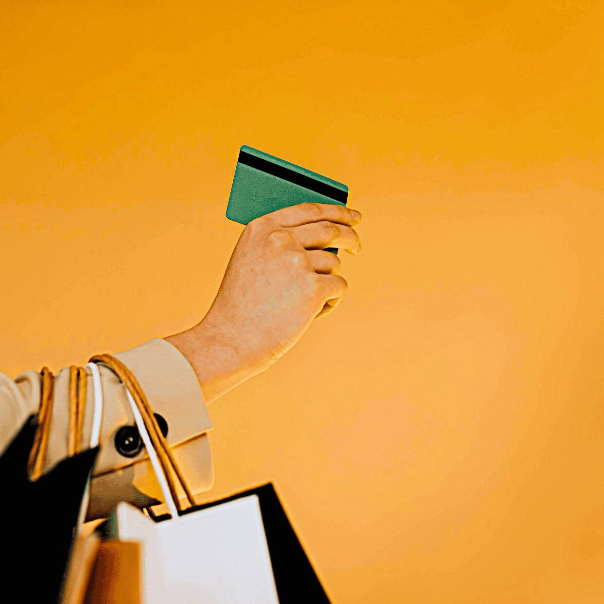 Person holding a credit card while carrying shopping bags against a bright background.