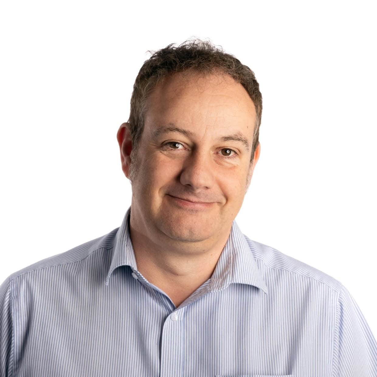 Smiling man wearing a light blue shirt against a plain background, professional headshot.