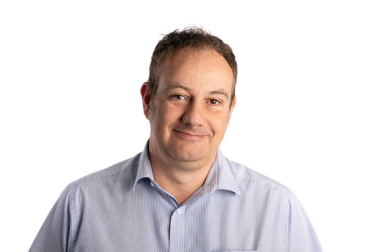 Smiling man wearing a light blue shirt against a plain background, professional headshot.