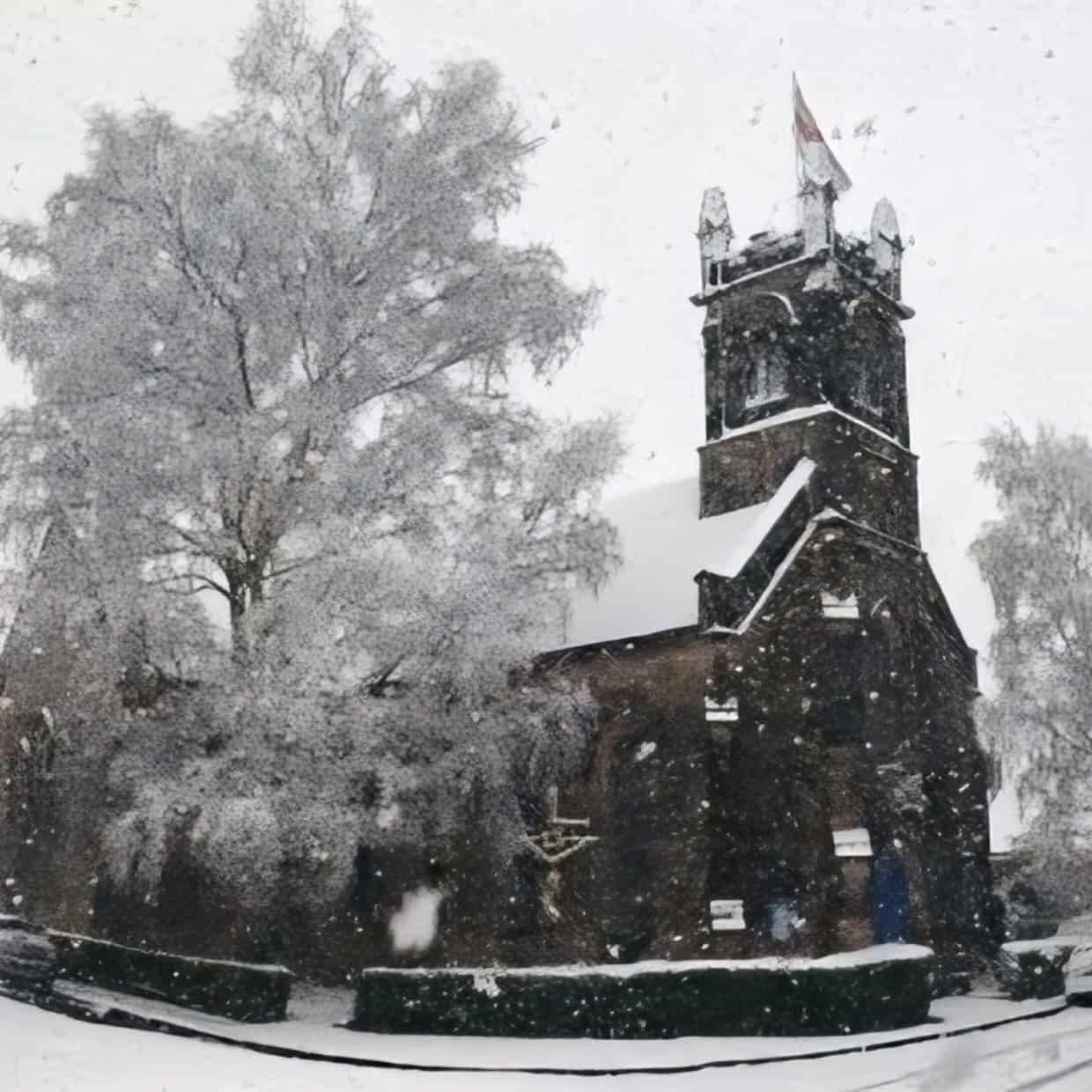 Traditional church building surrounded by trees during heavy snowfall in a winter scene.
