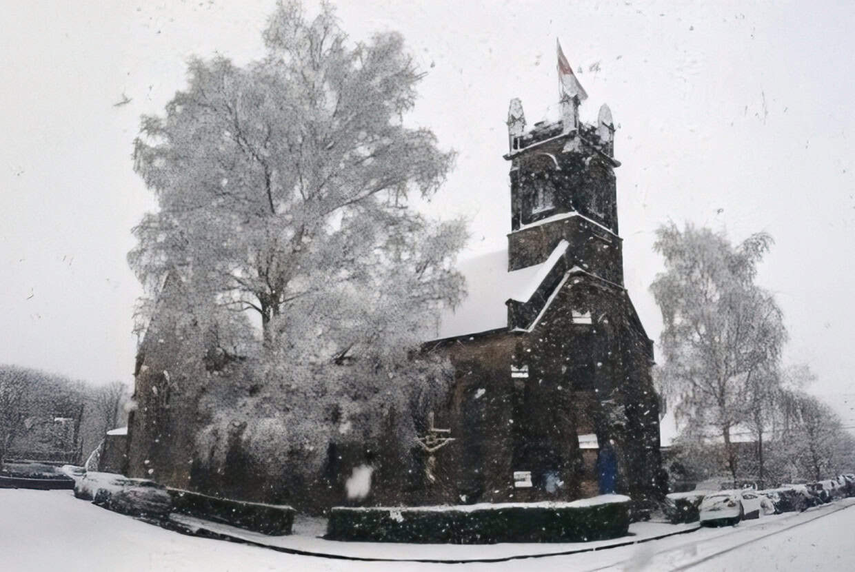 Traditional church building surrounded by trees during heavy snowfall in a winter scene.