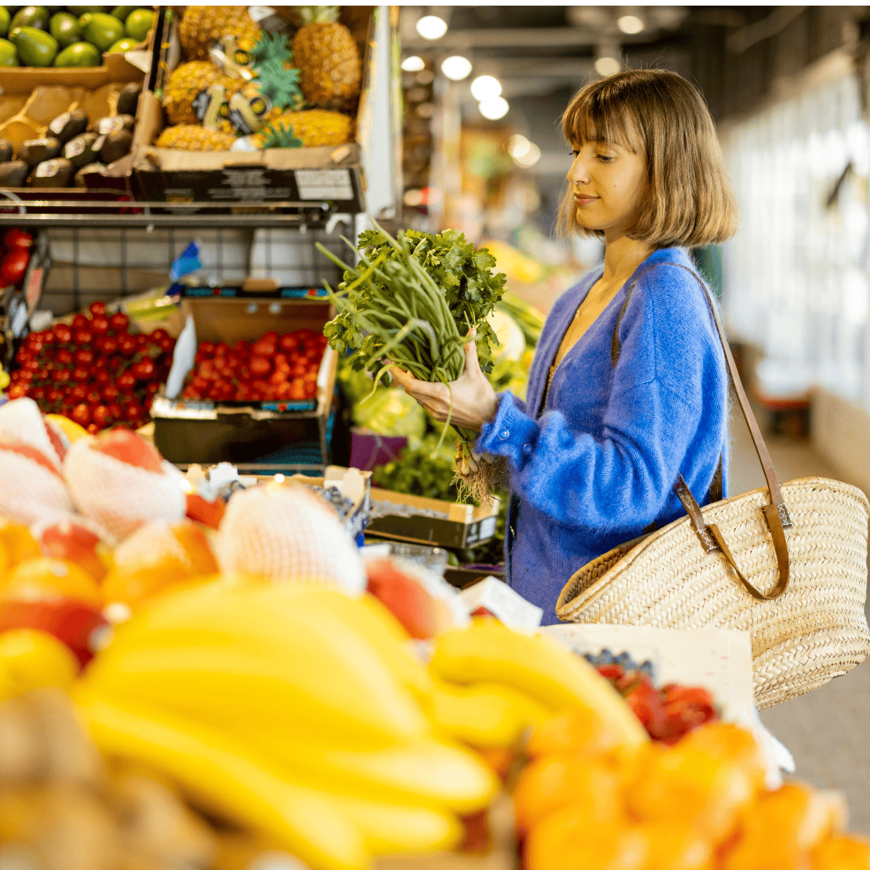Woman selecting fresh vegetables at a market stall with fruit and produce displayed around her.