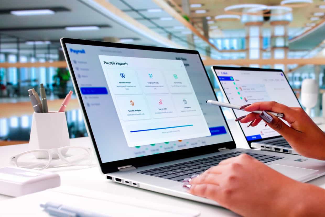 Person using a laptop to view payroll reports and financial data in a modern office setting.