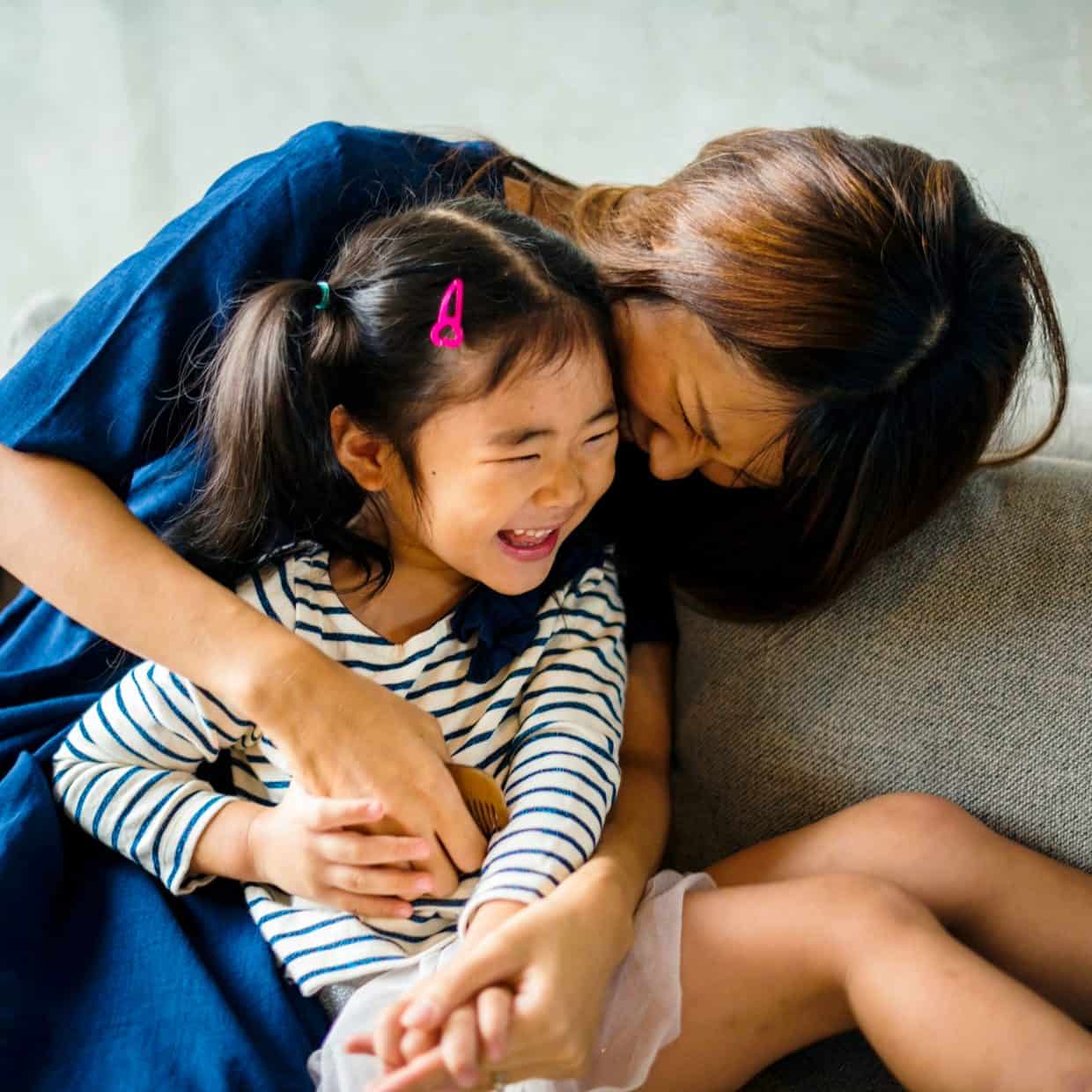 Mother and daughter laughing and cuddling together on a sofa at home.