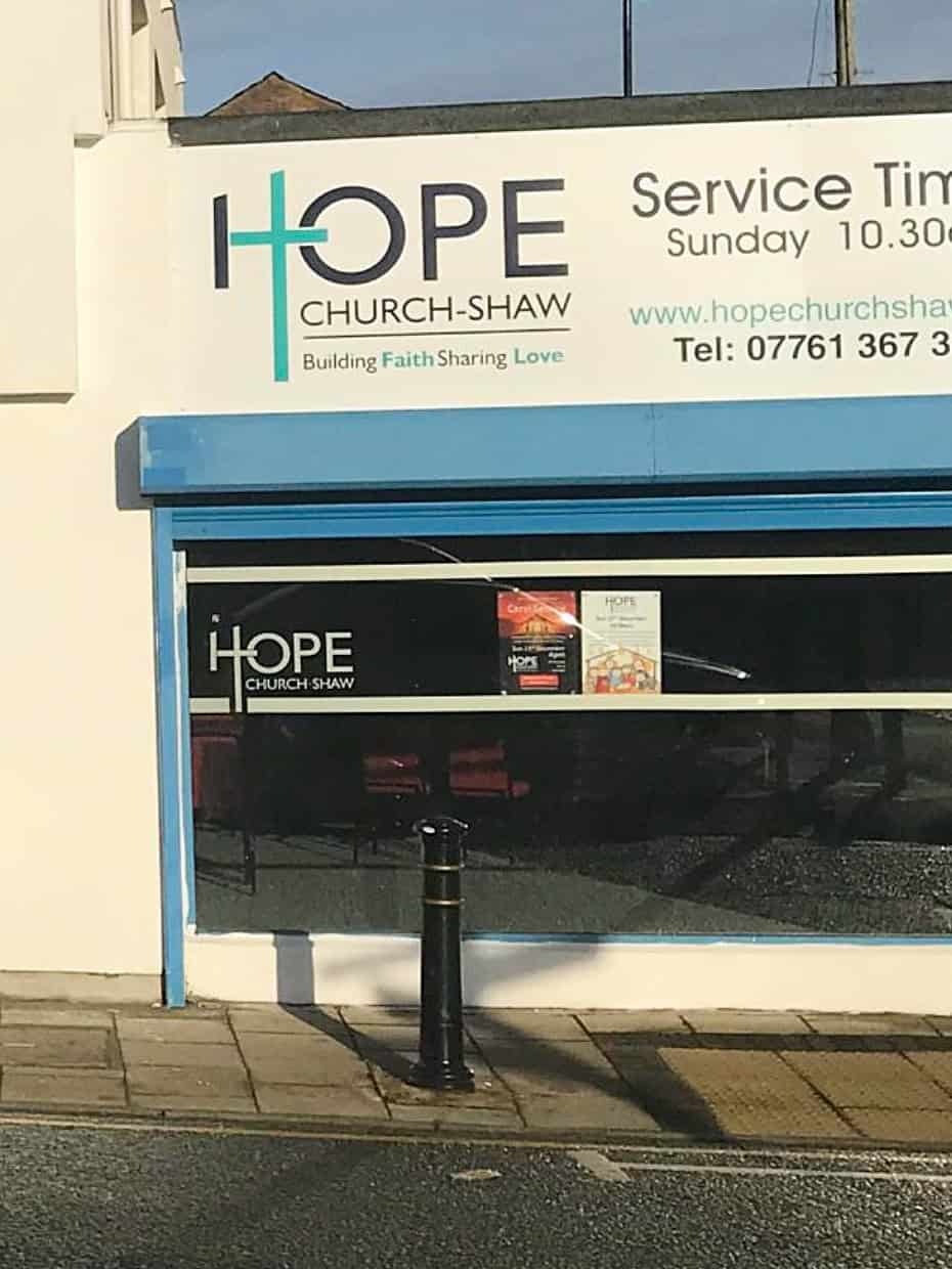 Exterior of Hope Church Shaw building with signage displaying service time of Sunday 10:30am, website address, and contact number above a blue-framed window.