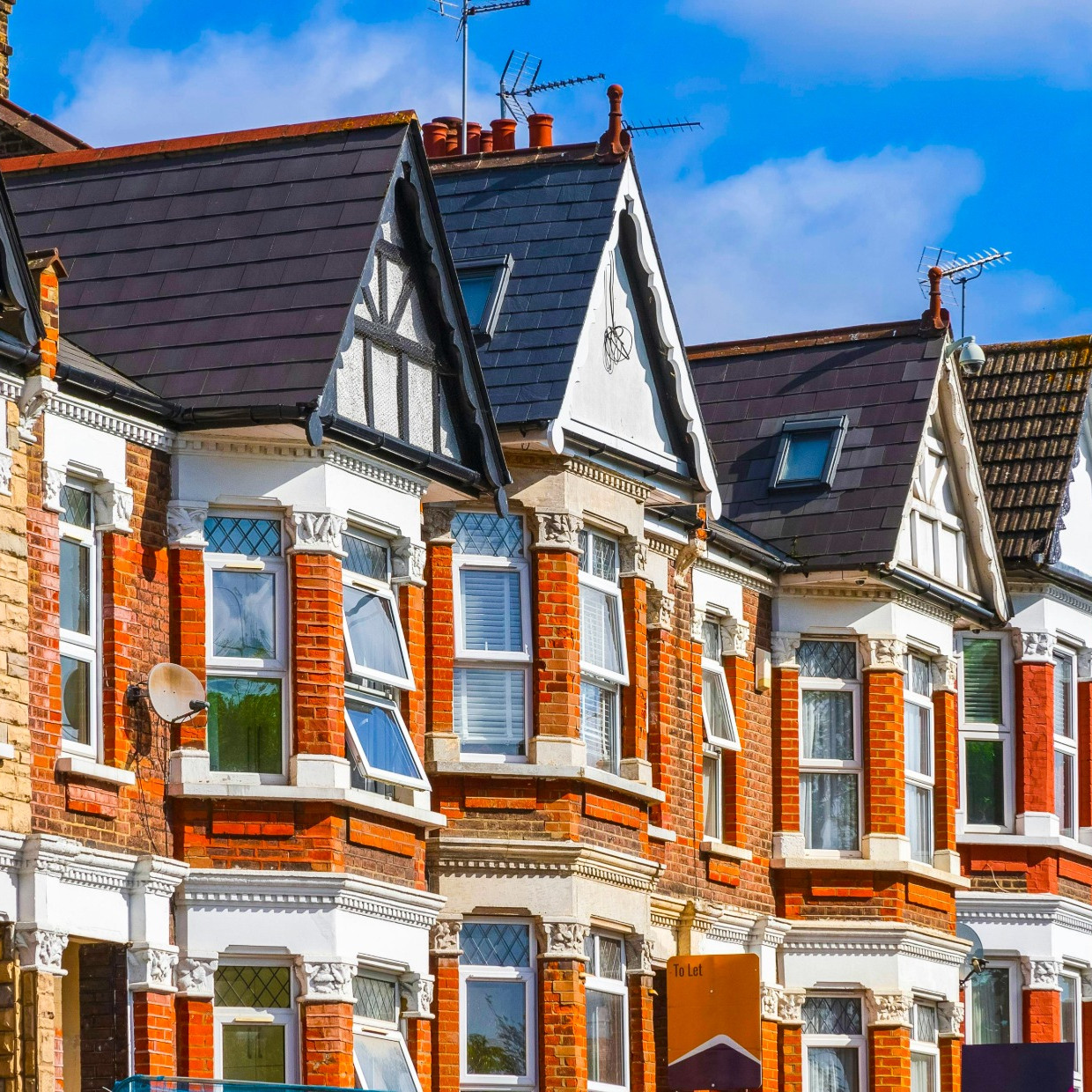 Row of Victorian terraced houses in the UK with red brick façades, bay windows, pitched slate roofs and decorative gables under a blue sky.