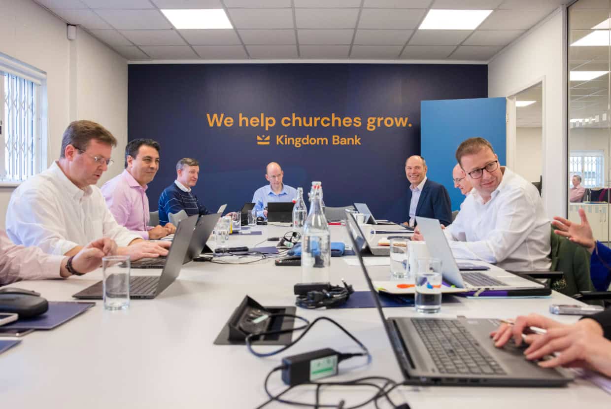 Kingdom Bank team meeting around a table with laptops, with the sign “We help churches grow."